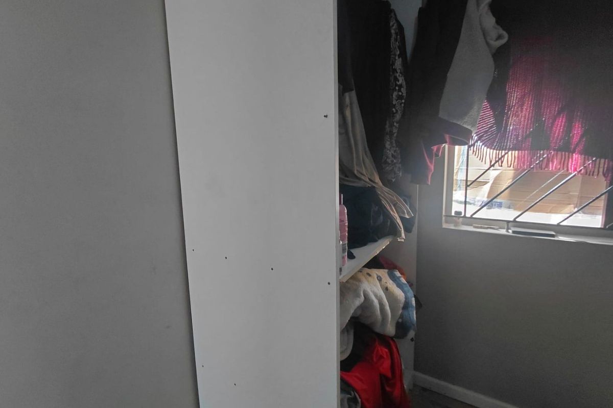 A view of a bedroom corner featuring a built-in cupboard and a window fitted with security bars.