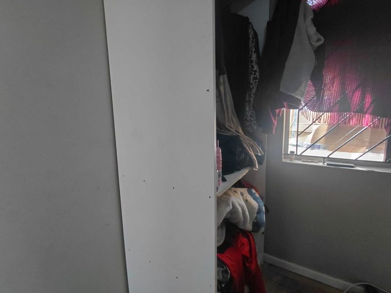 A view of a bedroom corner featuring a built-in cupboard and a window fitted with security bars.