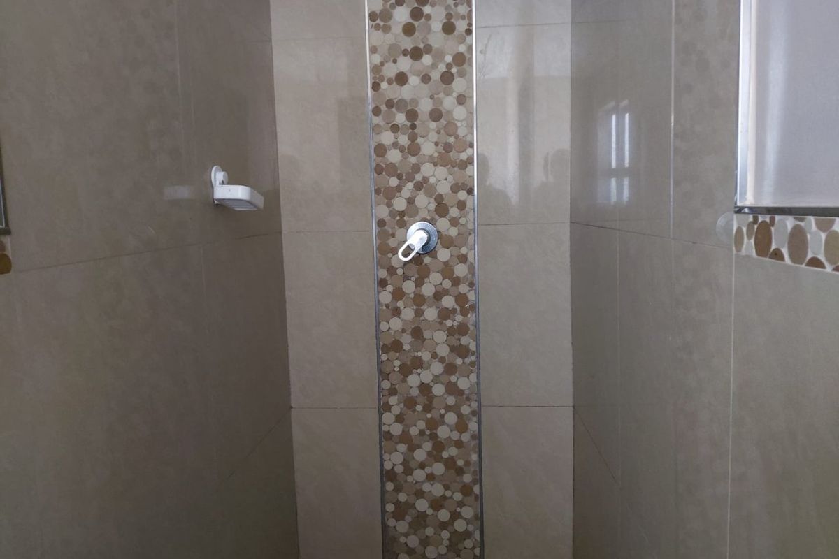 A clean shower enclosure featuring neutral wall tiles with a decorative mosaic accent strip and a built-in soap dish.