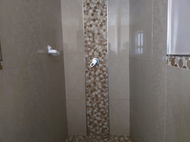 A clean shower enclosure featuring neutral wall tiles with a decorative mosaic accent strip and a built-in soap dish.