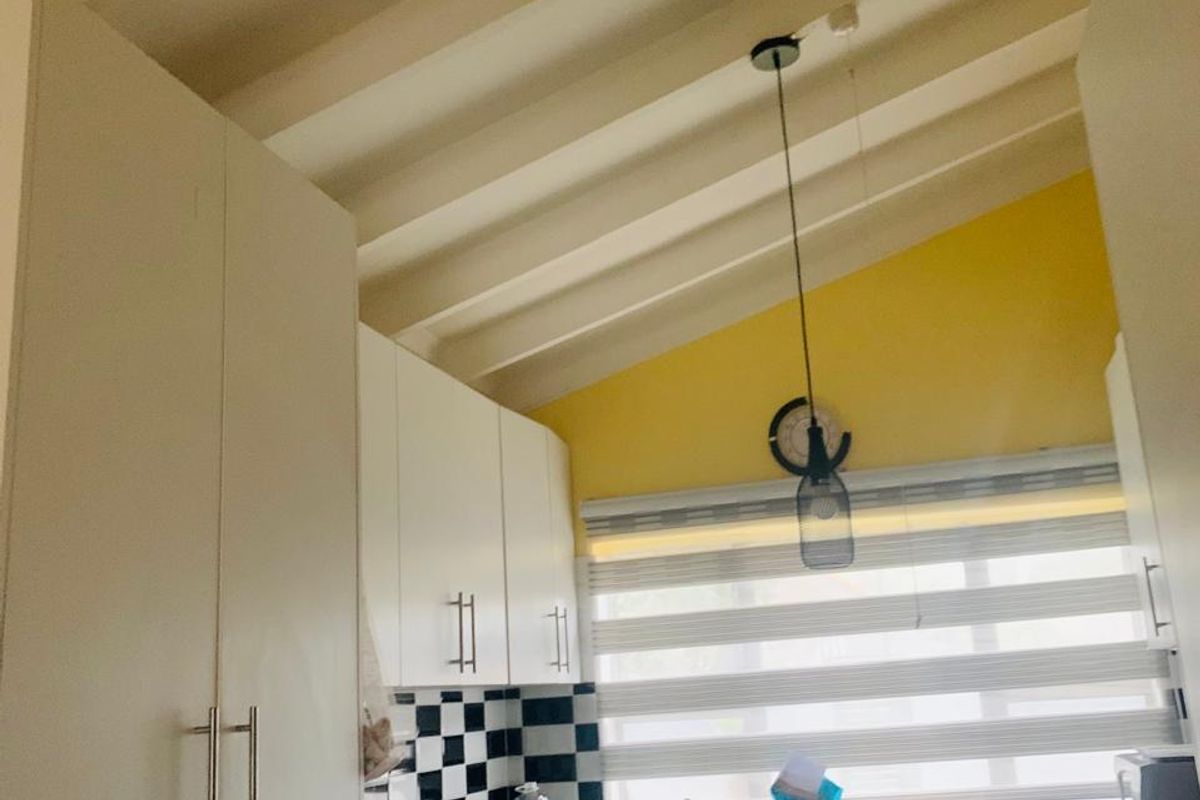 A functional kitchen featuring white cabinetry, black granite countertops, a checkered backsplash, and a distinctive vaulted ceiling with exposed beams.