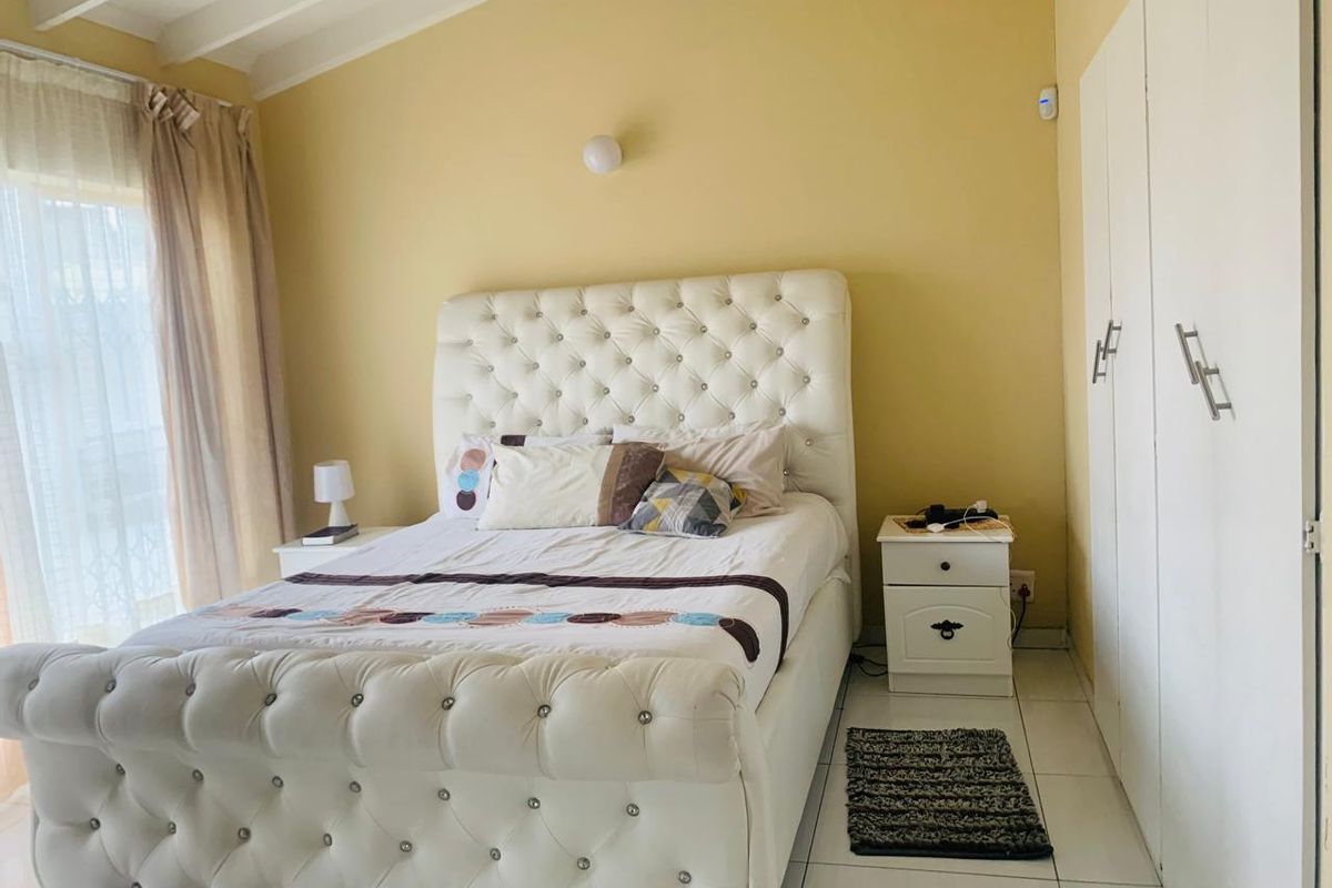 A bedroom featuring tiled flooring, built-in cupboards, and an exposed beam ceiling with yellow wall finishes.