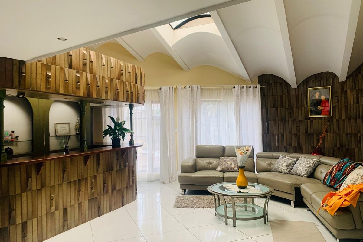 Spacious living area featuring a unique vaulted ceiling with skylight, tiled flooring, and a prominent built-in wooden bar unit.