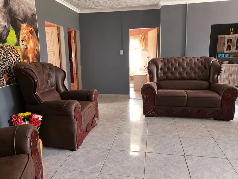 A living room featuring tiled flooring and textured ceiling, with visible surface-mounted electrical conduit and access to adjacent rooms.