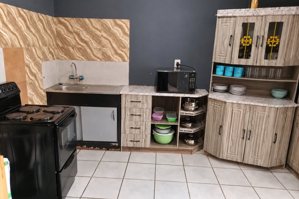 A functional kitchen featuring wood-look cabinetry, laminate countertops, a stainless steel sink, and a freestanding stove with tiled backsplash and flooring.