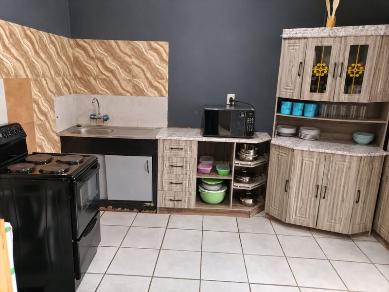 A functional kitchen featuring wood-look cabinetry, laminate countertops, a stainless steel sink, and a freestanding stove with tiled backsplash and flooring.