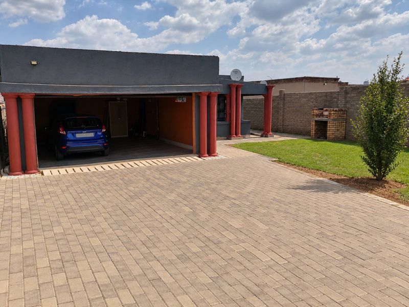Front exterior view featuring a paved driveway, double garage with decorative columns, and a brick built-in braai area in the garden.