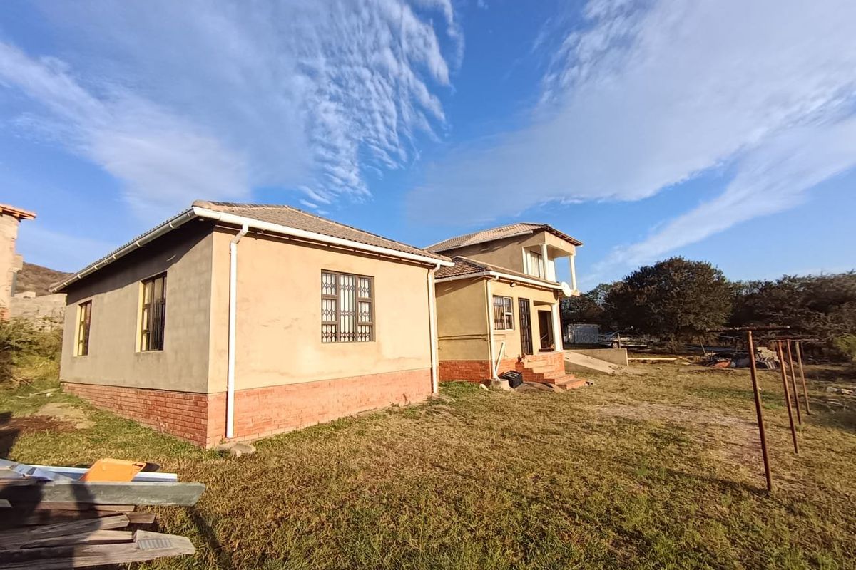 Rear view of a multi-level residential property featuring a tiled roof, brick base, and security bars on windows, set on a large plot.