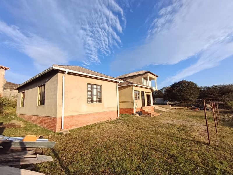 Rear view of a multi-level residential property featuring a tiled roof, brick base, and security bars on windows, set on a large plot.