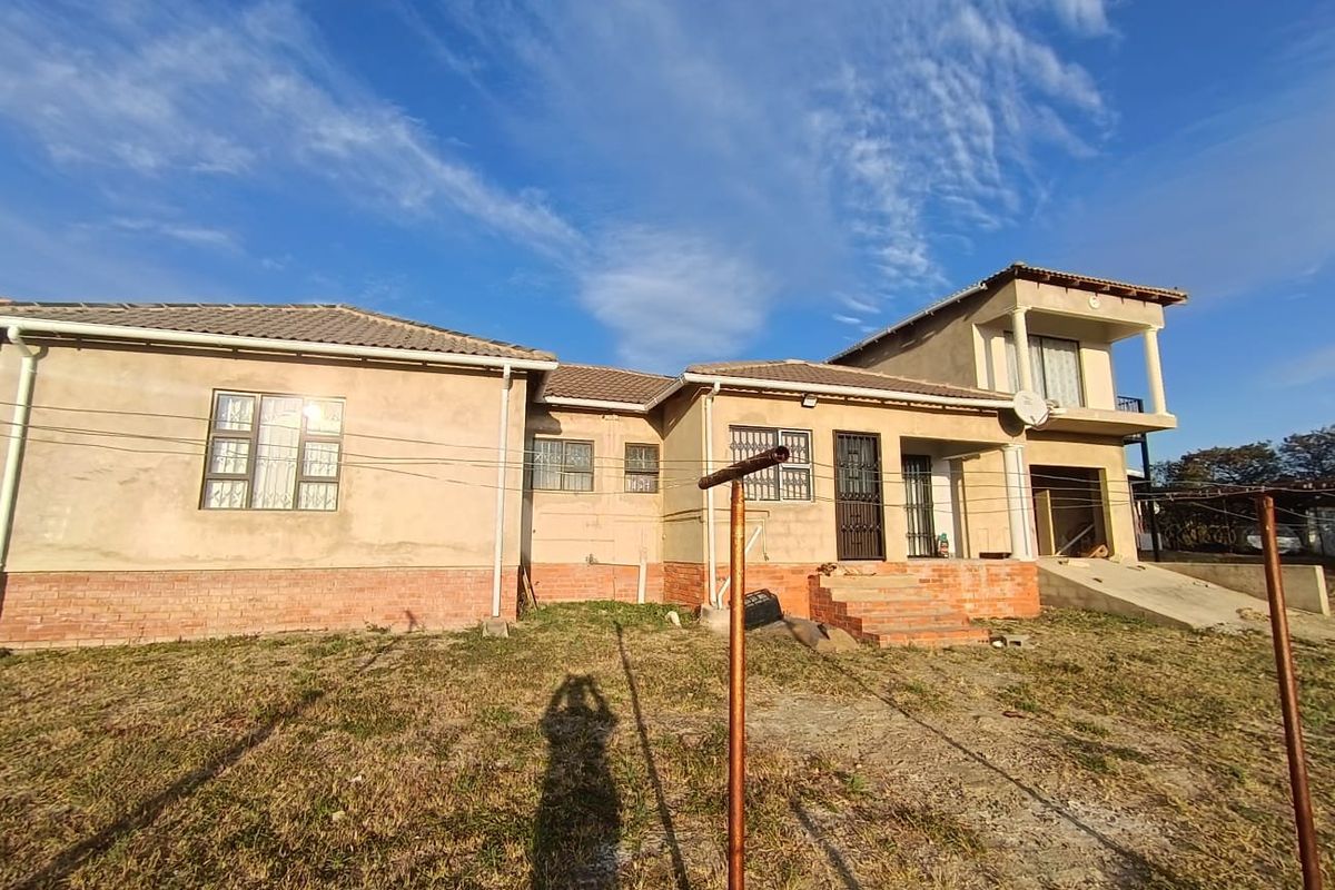 Rear view of a multi-level residential property featuring a tiled roof, balcony, and unfinished exterior plasterwork with a concrete ramp.