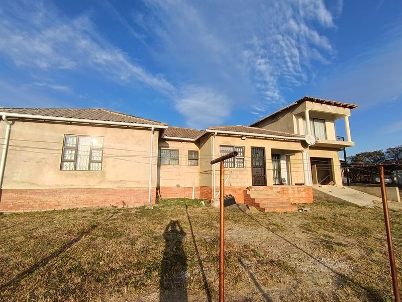 Rear view of a multi-level residential property featuring a tiled roof, balcony, and unfinished exterior plasterwork with a concrete ramp.