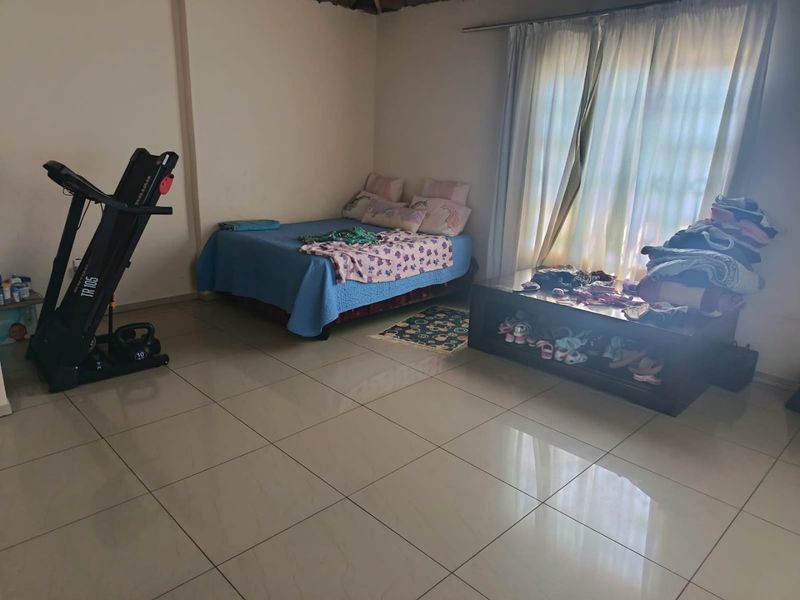 A bedroom featuring tiled flooring and a large window with a curtain rail, providing a functional space for rest.