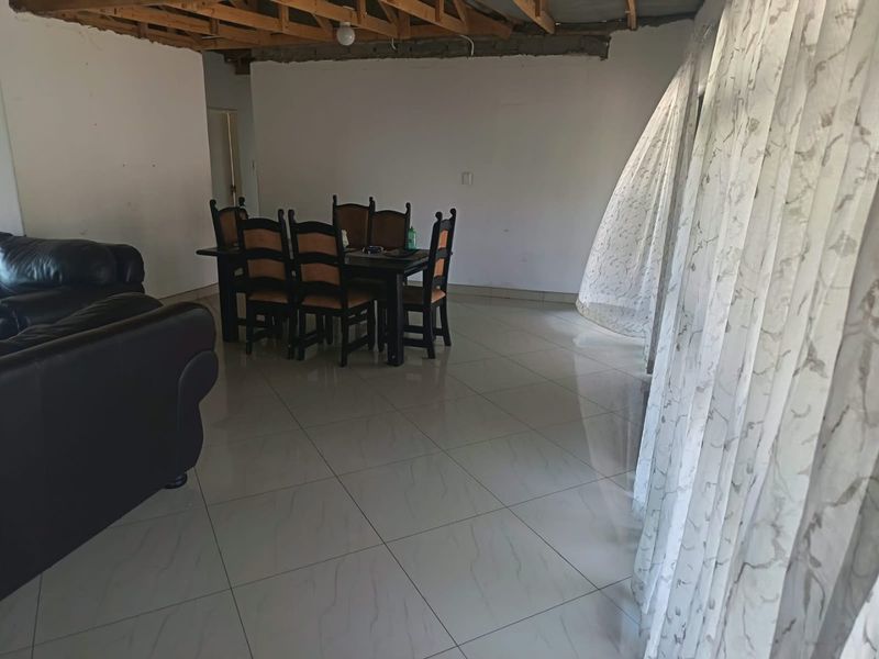 Open plan living and dining area featuring large format floor tiles and exposed timber roof trusses, requiring ceiling completion.
