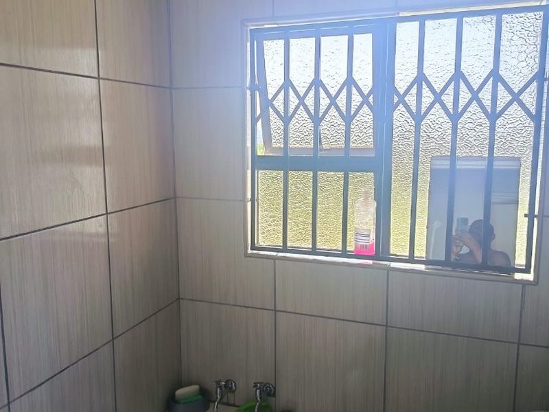 A functional bathroom featuring full-height wall tiling, a built-in bathtub, and a window fitted with a security gate.