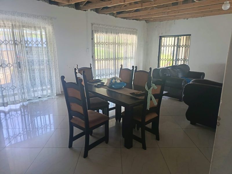 Open plan living and dining area featuring large format floor tiles, sliding doors with security gates, and an exposed timber beam ceiling requiring finishing.