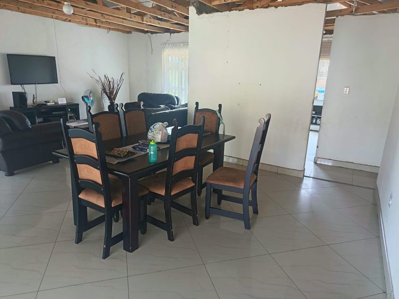 Open plan living and dining area featuring tiled flooring and exposed timber ceiling joists, currently requiring significant finishing and renovation work.