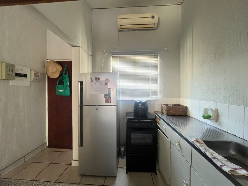 A functional kitchen area featuring built-in cabinetry, a stainless steel sink, tiled backsplash, and a wall-mounted air conditioning unit.