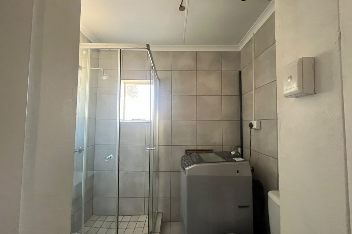 A compact bathroom featuring a glass shower enclosure, tiled finishes, and a toilet, requiring some cosmetic updates and electrical finishing.