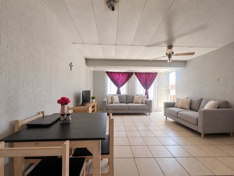 Spacious open-plan living and dining area featuring neutral tiled flooring, a ceiling fan, and textured walls with natural light from the sliding door.
