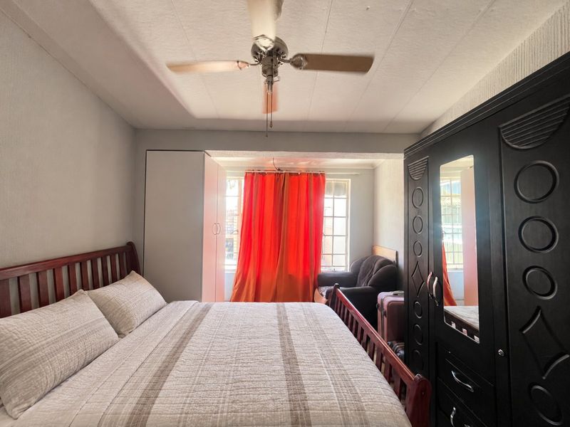 A functional bedroom featuring a ceiling fan and built-in wardrobe, offering a comfortable space with natural light from the window.