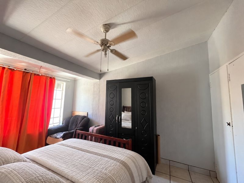 A functional bedroom featuring tiled flooring, a ceiling fan, and a built-in cupboard, offering a practical layout for comfortable living.
