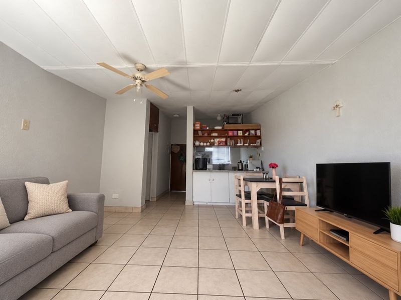 Open-plan living and dining area featuring tiled flooring, a ceiling fan, and a compact kitchen corner with built-in cabinetry.