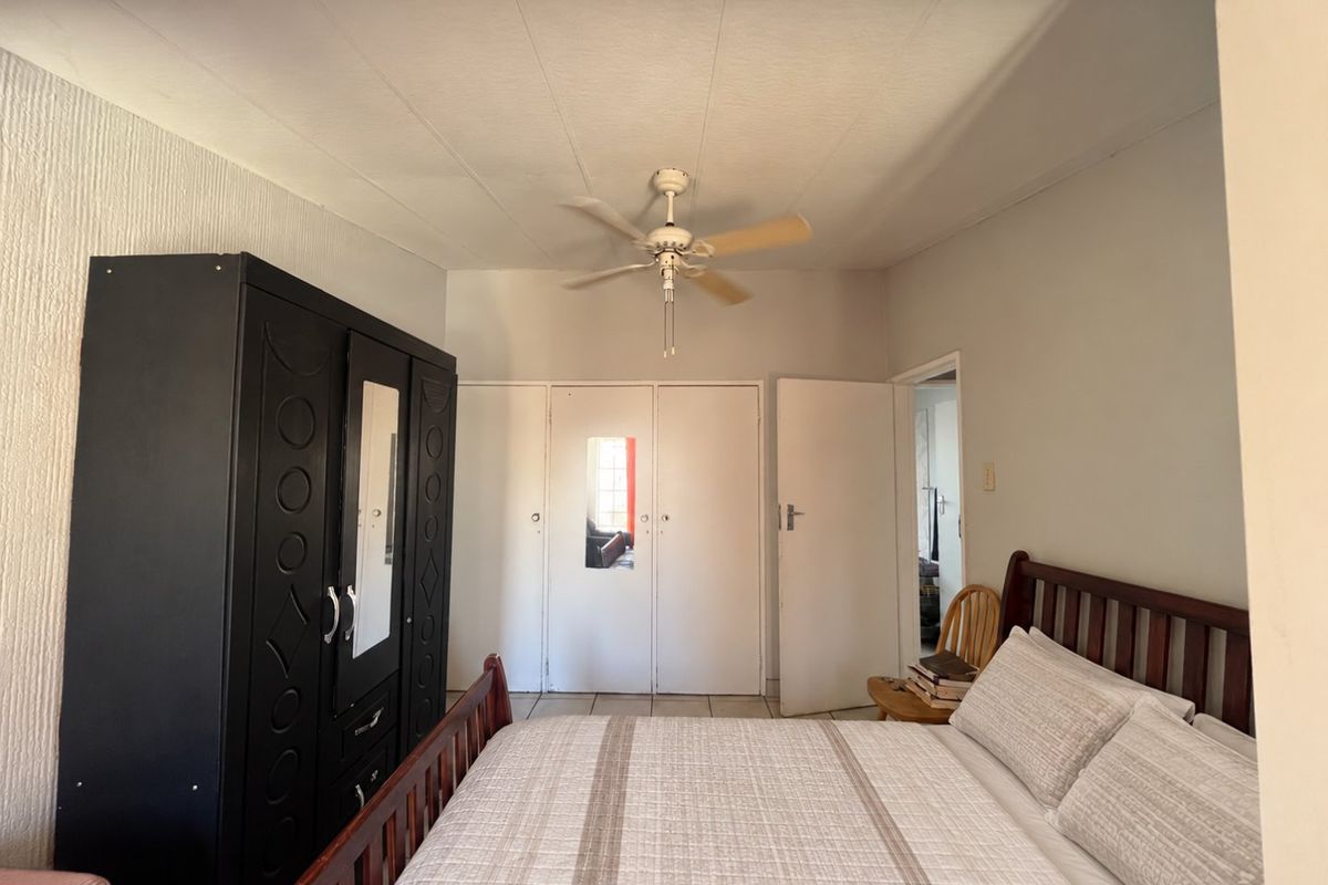 A bedroom featuring tiled flooring, a ceiling fan, and built-in cupboards providing ample storage space.