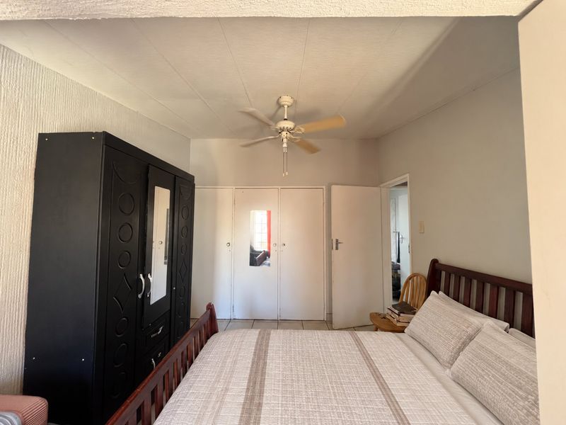 A bedroom featuring tiled flooring, a ceiling fan, and built-in cupboards providing ample storage space.