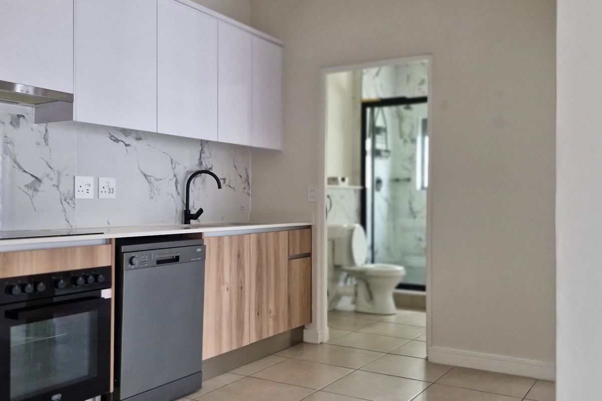 Modern kitchen featuring sleek white and wood-grain cabinetry, marble-look splashback, and integrated appliances, with a view into the adjacent bathroom.