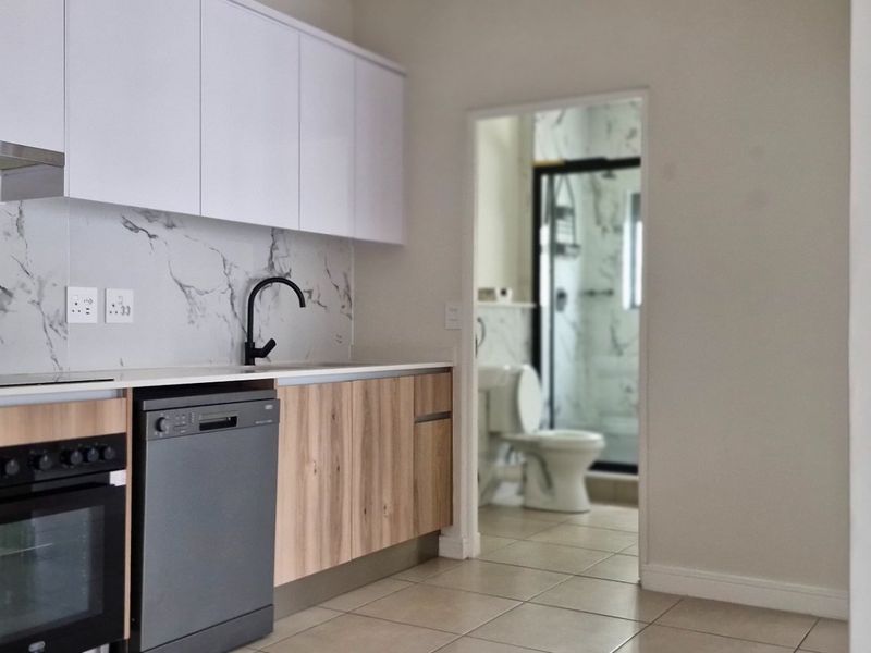 Modern kitchen featuring sleek white and wood-grain cabinetry, marble-look splashback, and integrated appliances, with a view into the adjacent bathroom.