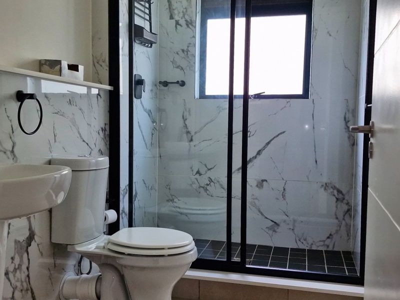 Modern bathroom featuring marble-look wall tiles, a pedestal basin, and a walk-in shower with a sleek black frame.