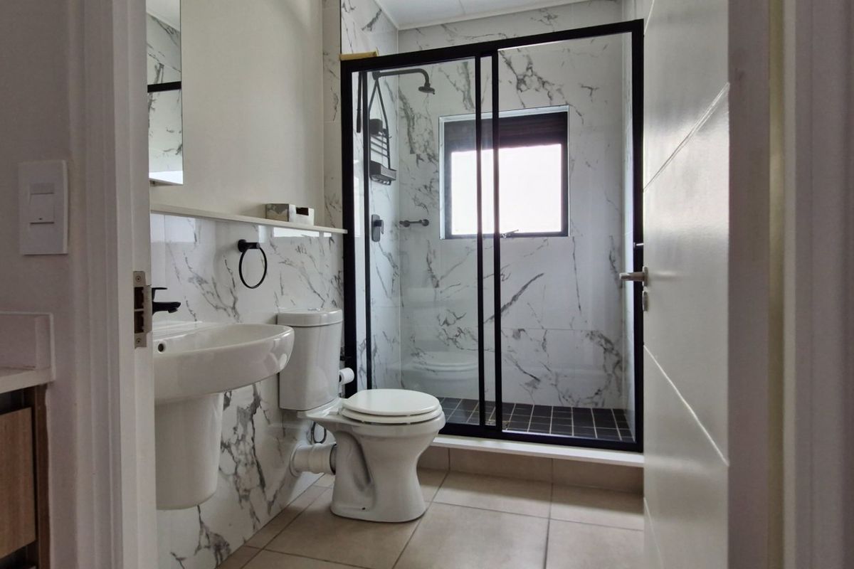 Modern bathroom featuring marble-effect wall tiles, a pedestal washbasin, a toilet, and a glass-enclosed shower with black frame detailing.