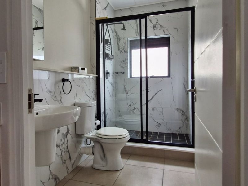 Modern bathroom featuring marble-effect wall tiles, a pedestal washbasin, a toilet, and a glass-enclosed shower with black frame detailing.