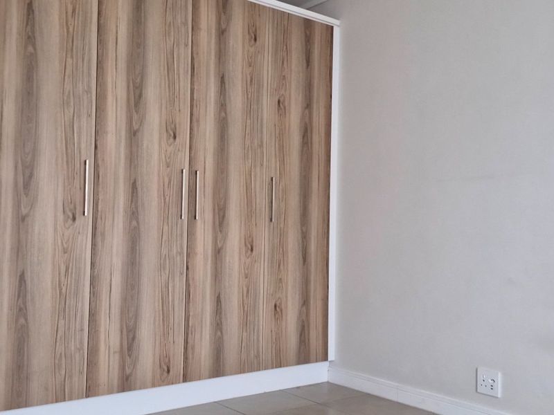 A clean, modern bedroom featuring neutral walls, tiled flooring, and ample built-in wooden cupboards with sleek handles.