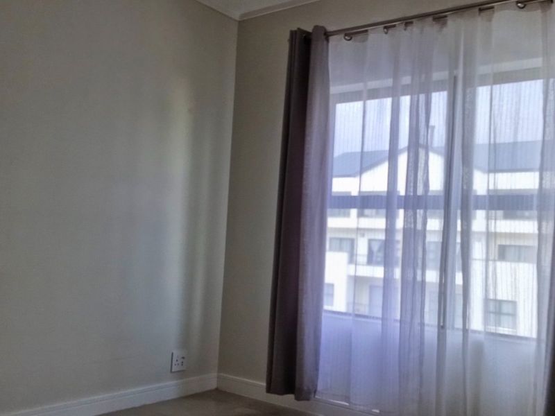 A bright, empty bedroom featuring neutral walls, carpeted flooring, and a window with installed curtain tracks.