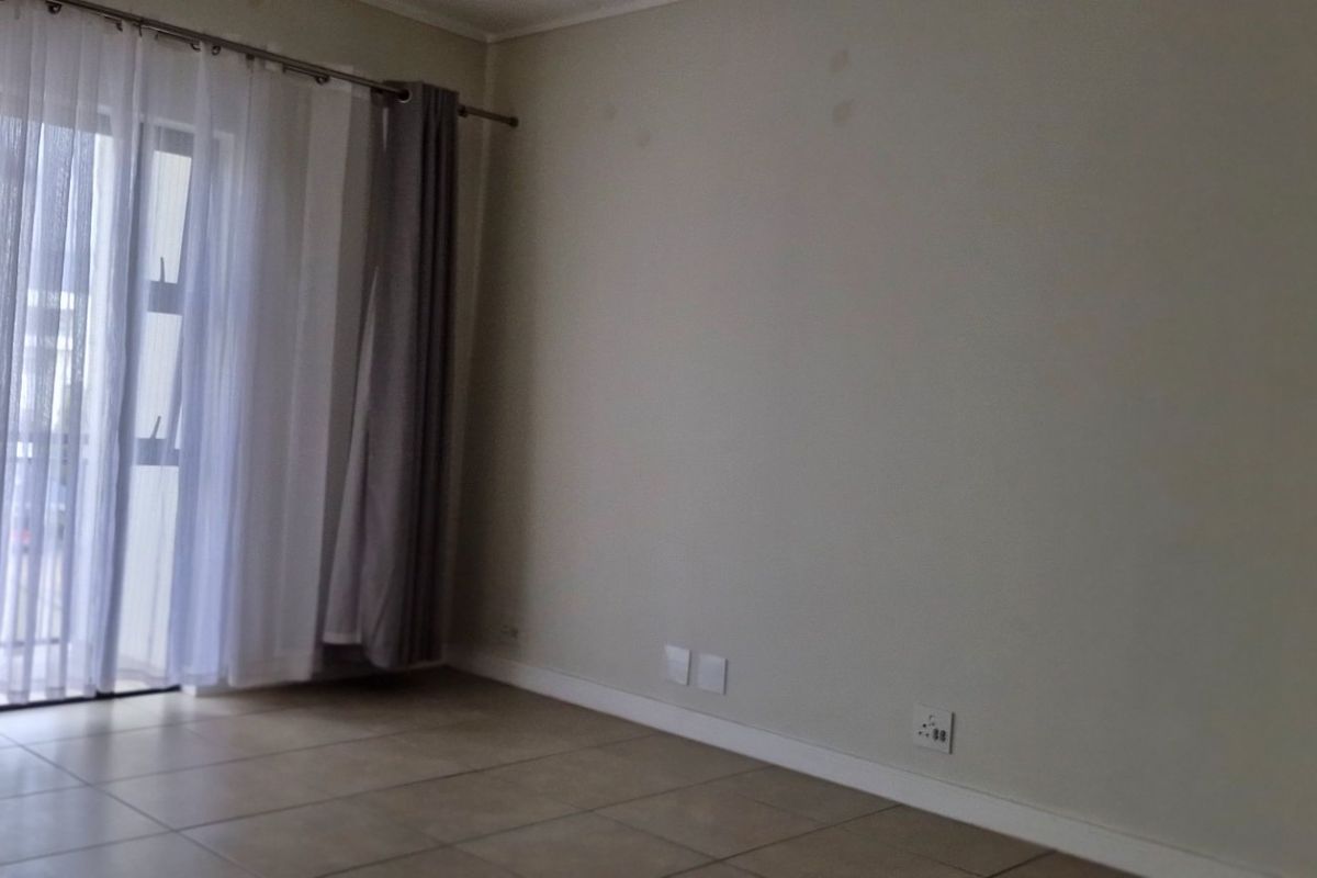 An empty living room featuring tiled flooring and a large sliding glass door providing access to the balcony.