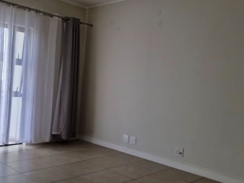 An empty living room featuring tiled flooring and a large sliding glass door providing access to the balcony.