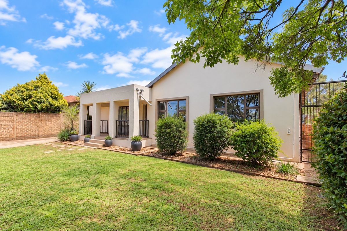 A well-maintained rear exterior view featuring a covered patio, landscaped garden, and secure boundary wall with aluminium window frames.