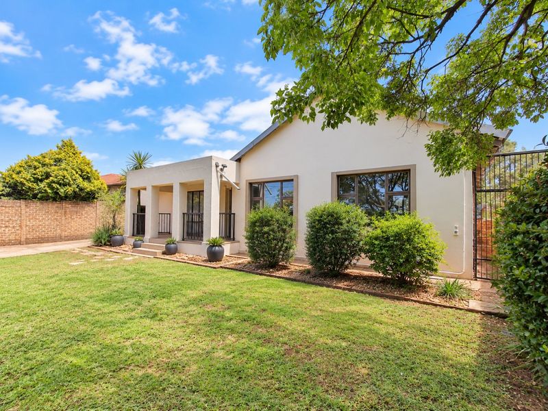 A well-maintained rear exterior view featuring a covered patio, landscaped garden, and secure boundary wall with aluminium window frames.