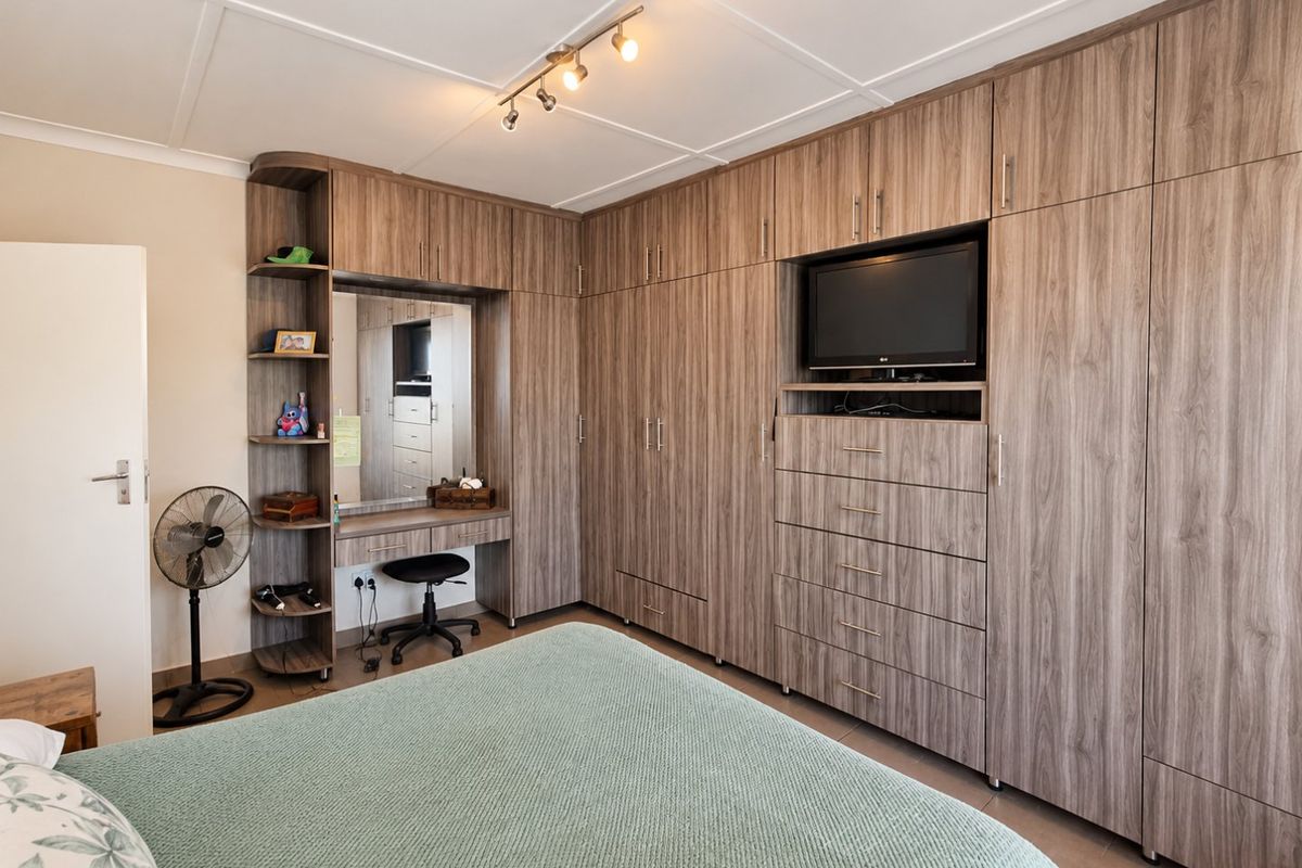 A well-maintained bedroom featuring extensive floor-to-ceiling built-in cabinetry with integrated vanity, shelving, and storage drawers.