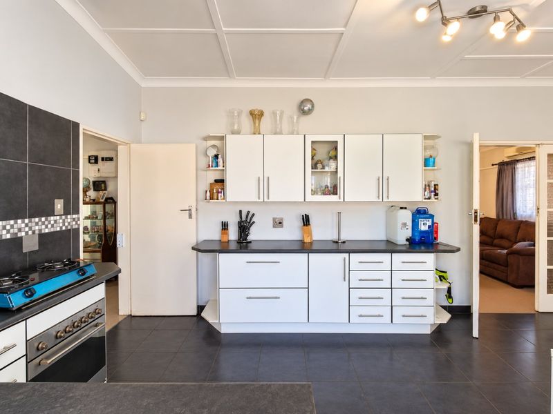 A functional kitchen featuring white cabinetry, dark countertops, a gas stove, and tiled flooring, with direct access to adjacent living areas.