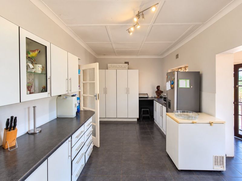 Functional kitchen featuring white cabinetry, dark laminate countertops, tiled flooring, and ample built-in storage space with direct access to the exterior.