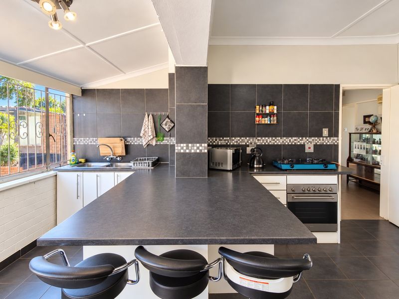 A functional kitchen featuring a large breakfast bar, dark tiled backsplash, built-in oven with gas hob, and a double sink with window views.