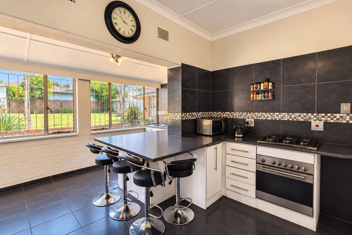 A functional kitchen featuring a breakfast bar, built-in oven, gas cooktop, and dark tiled flooring, with large windows overlooking the garden.