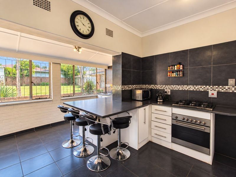 A functional kitchen featuring a breakfast bar, built-in oven, gas cooktop, and dark tiled flooring, with large windows overlooking the garden.