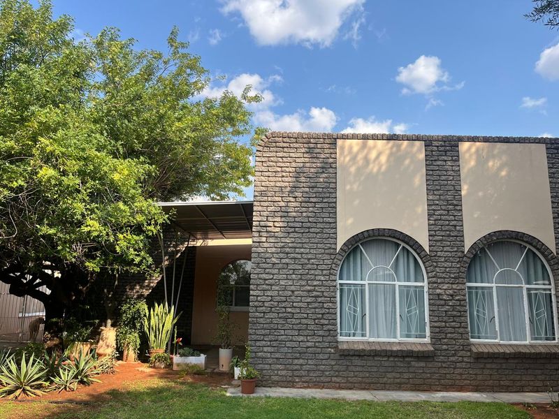 Front elevation of a house featuring a textured face brick facade, arched windows, and a covered patio area set within a landscaped garden.