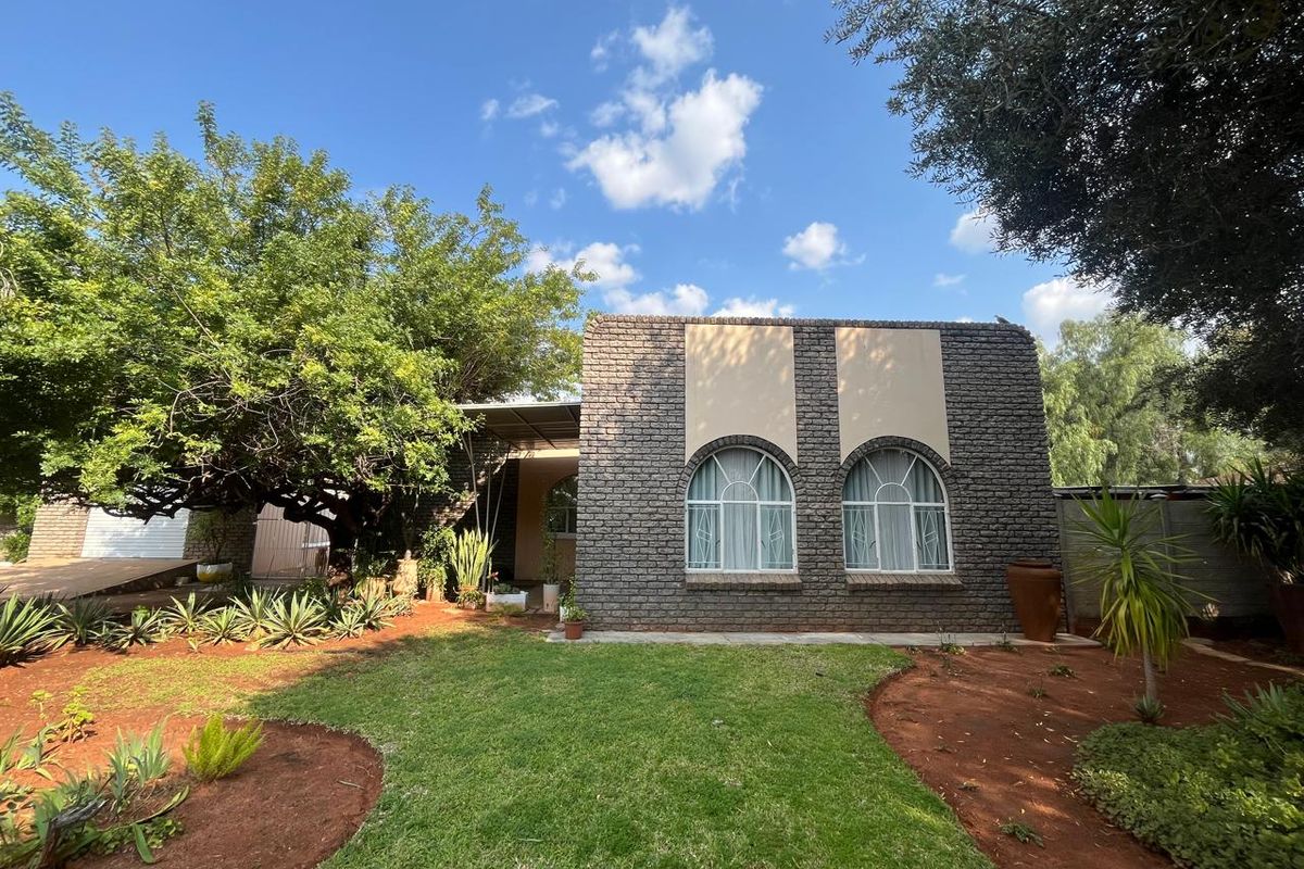 A well-maintained rear exterior view of the house featuring a brick facade, arched windows, and a landscaped garden with mature trees.