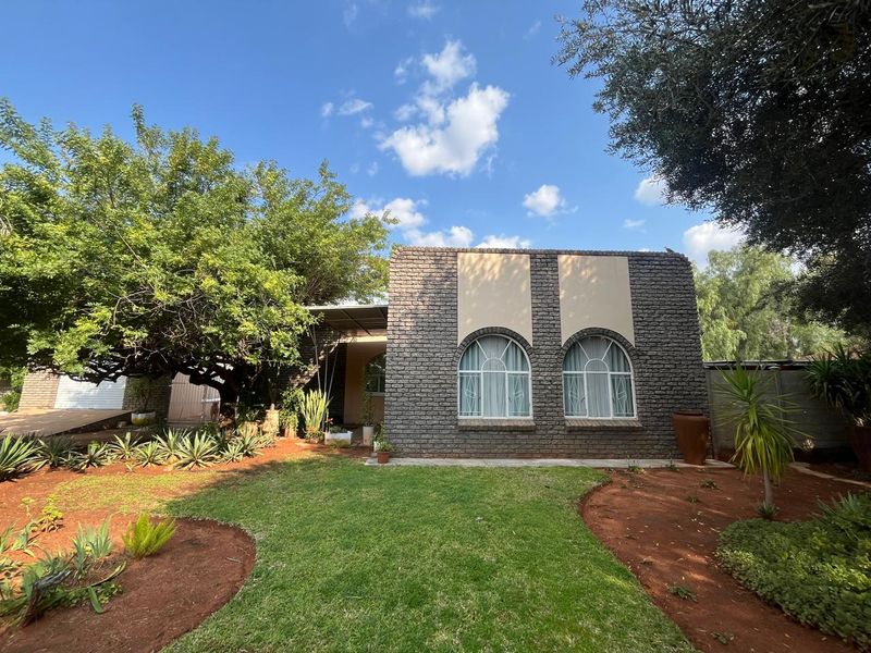 A well-maintained rear exterior view of the house featuring a brick facade, arched windows, and a landscaped garden with mature trees.