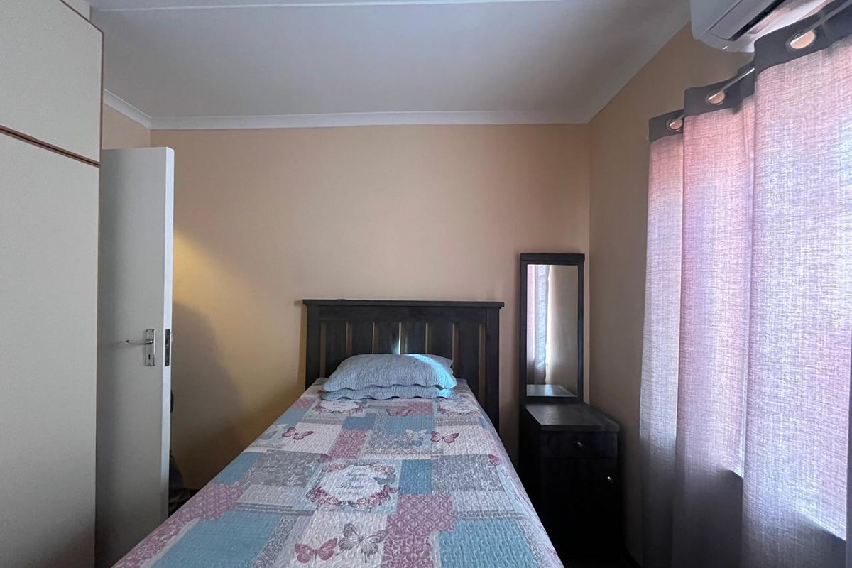 A functional bedroom featuring a built-in cupboard, coved ceiling, and a wall-mounted air conditioning unit.