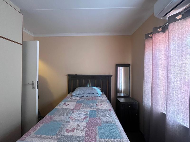 A functional bedroom featuring a built-in cupboard, coved ceiling, and a wall-mounted air conditioning unit.